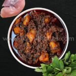 Bowl of hearty beef and potato stew in a dark sauce, with fresh herbs nearby on a black surface.