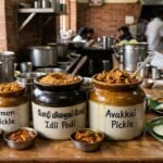 Row of ceramic jars labeled Garlic Podi, Lemon Pickle, Idli Podi, and Avakkai Pickle on a wooden counter in an Indian eatery.